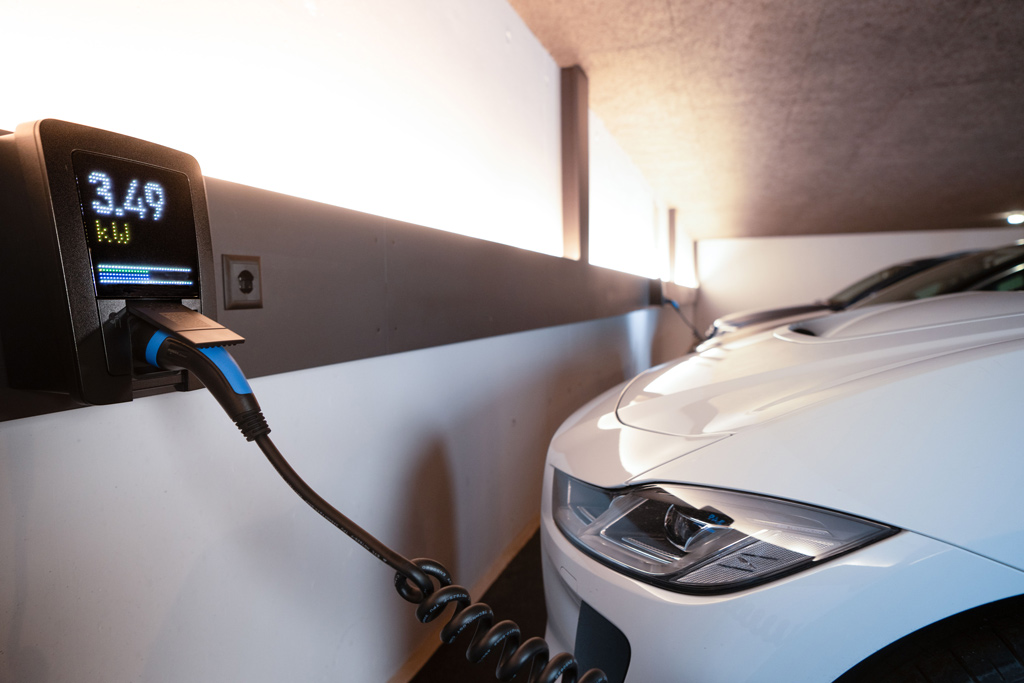 Carregador wallbox instalado em parede de garagem, com display indicando a potência de carga e cabo conectado a um carro elétrico