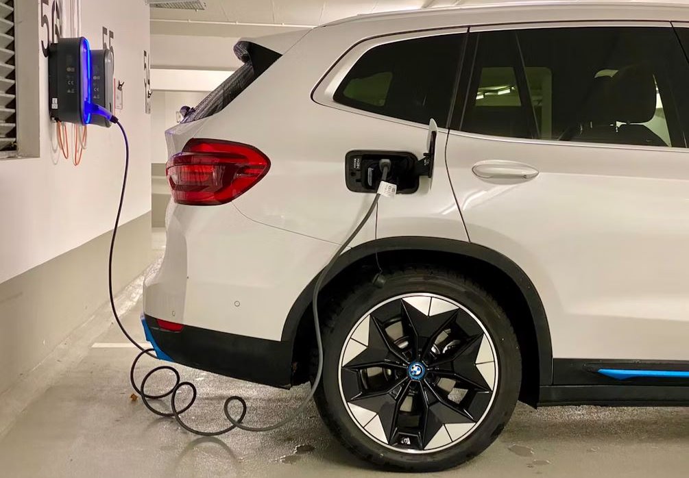 Carro elétrico carregando em vaga de garagem de condomínio, com wallbox fixado na parede e cabo conectado ao veículo